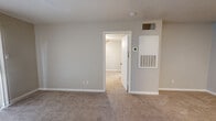 This efficient single-floor unit is thoughtfully laid out to maximize every square foot of its compact footprint. The combined living and dining area serves as the heart of the home, featuring neutral-toned carpet, soft beige walls, and a front entry door with a side window dressed in vertical blinds that allow natural light to filter in. A ceiling fan with integrated lighting adds both comfort and functionality to this shared living space.

The galley-style kitchen is well-appointed with white upper cabinetry, light countertops, a stainless sink, and wood-look vinyl flooring. Black appliances, including a refrigerator and range, provide a clean contrast to the lighter finishes throughout.

The bedroom is a comfortable, carpeted retreat featuring a window with blinds that brings in natural light and a ceiling fan overhead. It connects directly to a dedicated walk-in closet outfitted with multiple shelving tiers and hanging rods, offering ample storage capacity.

The full bathroom includes wood-look vinyl flooring, a speckled granite-style vanity countertop with an undermount sink, a toilet, and a full shower-tub combination with white tile surround. An overhead shelf adds extra storage above the vanity area. The unit also features a wall-mounted HVAC unit and a thermostat conveniently located in the bedroom area, ensuring year-round climate control.