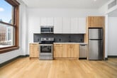 This thoughtfully designed one-bedroom, one-bathroom residence offers a efficient and modern living experience across a single floor. Light hardwood flooring flows throughout the open layout, creating a cohesive and contemporary aesthetic.

The open living area and kitchen occupy a shared space anchored by large, double-hung windows with rich, dark wood framing that frame sweeping city views. A ceiling fan with integrated lighting serves the bedroom, which also benefits from the same bold-trimmed windows, flooding the room with natural light and urban scenery.

The kitchen is appointed with two-tone cabinetry — white upper cabinets paired with light wood lower cabinets — complemented by a dark penny-tile backsplash, white quartz countertops, and a full suite of stainless steel appliances including a range, microwave, dishwasher, and refrigerator. A matte black faucet adds a refined finishing touch.

The bathroom features penny-tile flooring, a full tub-shower combination with white subway tile surround and a built-in niche, a wood-toned vanity, and a bold dark accent wall. A dedicated laundry room provides an in-unit washer-dryer combo with wire shelving above for additional storage. A central hallway connects all rooms and includes an electrical panel access point.