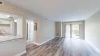 This single-floor residence has been thoughtfully updated with a cohesive palette of warm neutral tones and wood-look luxury vinyl plank flooring that flows consistently throughout the space. The open living area is a standout feature, anchored by a sliding glass door framed with sheer vertical blinds that invite natural light and provide views of lush outdoor greenery, creating a bright and airy atmosphere.

The galley-style kitchen is well-appointed with crisp white shaker cabinetry, light granite countertops, stainless steel appliances including a range and refrigerator, and a tray ceiling detail that adds subtle architectural interest. A window above allows for additional natural light.

The bathroom showcases updated finishes, including large-format marble-patterned tile lining the walk-in shower with a pebble stone floor, a white vanity topped with matching granite, and coordinating fixtures throughout.

The bedrooms are comfortably sized, each featuring windows fitted with white blinds that allow for controlled natural light. Clean walls in warm beige tones and consistent flooring maintain a unified aesthetic. The entry area provides a welcoming introduction to the space, with recessed lighting and a pass-through detail connecting to adjacent rooms.