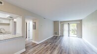 This single-floor residence has been thoughtfully updated with a cohesive palette of warm neutral tones and wood-look luxury vinyl plank flooring that flows consistently throughout the space. The open living area is a standout feature, anchored by a sliding glass door framed with sheer vertical blinds that invite natural light and provide views of lush outdoor greenery, creating a bright and airy atmosphere.

The galley-style kitchen is well-appointed with crisp white shaker cabinetry, light granite countertops, stainless steel appliances including a range and refrigerator, and a tray ceiling detail that adds subtle architectural interest. A window above allows for additional natural light.

The bathroom showcases updated finishes, including large-format marble-patterned tile lining the walk-in shower with a pebble stone floor, a white vanity topped with matching granite, and coordinating fixtures throughout.

The bedrooms are comfortably sized, each featuring windows fitted with white blinds that allow for controlled natural light. Clean walls in warm beige tones and consistent flooring maintain a unified aesthetic. The entry area provides a welcoming introduction to the space, with recessed lighting and a pass-through detail connecting to adjacent rooms.