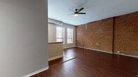 Located at 330 W Fourth St in the heart of downtown Cincinnati, Ohio, this single-floor unit blends industrial character with modern finishes throughout. Rich, dark hardwood-style flooring runs continuously across the entire space, anchoring each room with warmth and cohesion.

The open living area is a standout, showcasing a full wall of exposed red brick that adds striking texture and historic urban character. Multiple windows invite natural light, while a ceiling fan overhead provides comfort and airflow. The layout flows naturally into a kitchen outfitted with white shaker-style cabinetry, dark countertops, a stainless steel gas range, over-the-range microwave, dishwasher, and refrigerator. A peninsula-style counter separates the kitchen from the living area, offering casual seating and additional workspace. Large windows in the kitchen area further brighten the space.

The bedroom areas feature neutral gray walls, clean lines, and continued hardwood-style flooring. One bedroom includes tall ceilings with exposed structural beams and generous windows overlooking the surrounding cityscape. The bathroom is clean and functional, featuring a full tub-shower combination, white vanity, and consistent flooring that ties the space together. The overall ambiance is modern-industrial, well-suited to urban living in one of Cincinnati's most central neighborhoods.