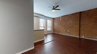 Located at 330 W Fourth St in the heart of downtown Cincinnati, Ohio, this single-floor unit blends industrial character with modern finishes throughout. Rich, dark hardwood-style flooring runs continuously across the entire space, anchoring each room with warmth and cohesion.

The open living area is a standout, showcasing a full wall of exposed red brick that adds striking texture and historic urban character. Multiple windows invite natural light, while a ceiling fan overhead provides comfort and airflow. The layout flows naturally into a kitchen outfitted with white shaker-style cabinetry, dark countertops, a stainless steel gas range, over-the-range microwave, dishwasher, and refrigerator. A peninsula-style counter separates the kitchen from the living area, offering casual seating and additional workspace. Large windows in the kitchen area further brighten the space.

The bedroom areas feature neutral gray walls, clean lines, and continued hardwood-style flooring. One bedroom includes tall ceilings with exposed structural beams and generous windows overlooking the surrounding cityscape. The bathroom is clean and functional, featuring a full tub-shower combination, white vanity, and consistent flooring that ties the space together. The overall ambiance is modern-industrial, well-suited to urban living in one of Cincinnati's most central neighborhoods.