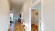 This single-floor residence is thoughtfully designed with an open, airy layout and consistent use of light hardwood flooring and neutral tones throughout. The living room commands attention with soaring vaulted ceilings and a large sliding glass door that draws in natural light and frames outdoor green views, creating a bright and welcoming atmosphere.

The kitchen is a functional centerpiece of the home, featuring white shaker cabinetry, a subway tile backsplash, stainless steel appliances, and a generous island with seating for multiple guests. Pendant lighting overhead adds a contemporary touch. An adjacent dining area offers additional space for entertaining, complete with a ceiling fan and a large window.

A dedicated office provides a quiet workspace with carpet flooring, a ceiling fan, and a window overlooking the outdoors. The bedroom is a comfortable retreat, also carpeted, with multiple windows allowing natural light and a ceiling fan for comfort. It connects to a walk-in closet with built-in shelving for organized storage.

The bathroom is finished with a dual-sink vanity featuring white cabinetry and brushed nickel hardware, a combined tub and shower with a glass enclosure, and light hardwood-style flooring, delivering a clean, modern aesthetic throughout.