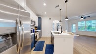 Located at 22100 E Quincy Ave in Aurora, CO, this thoughtfully designed one-bedroom, one-bathroom residence offers a well-appointed layout across a single floor. The open-concept kitchen is a true centerpiece, showcasing bold two-tone cabinetry with navy blue lower cabinets and crisp white uppers, quartz countertops, a hexagonal tile backsplash, stainless steel appliances, and a spacious island with a matte black faucet and pendant lighting — ideal for both cooking and casual dining. Light wood-tone flooring flows seamlessly throughout, enhancing the bright, airy atmosphere created by recessed lighting and an arched pass-through detail. The living room is generously proportioned, bathed in natural light from large windows, and features a ceiling fan and direct access to a private balcony. The bedroom offers a comfortable retreat with a walk-in closet featuring built-in shelving, a ceiling fan, and a sun-filled window with outdoor views. The bathroom is finished with large-format tile surrounding a soaking tub and is complemented by a vanity with modern fixtures. Additional conveniences include in-unit laundry, a pantry, and utility storage, rounding out this efficient and stylish residence.