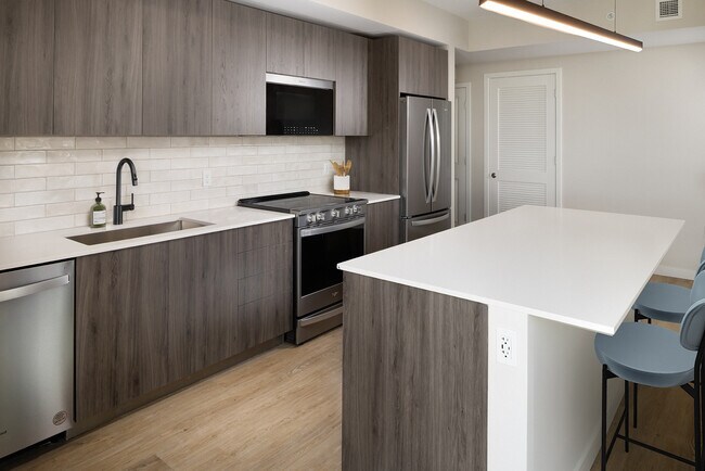 Colección Upgrade II Cocina de apartamento de tres habitaciones con gabinetes color espresso, placa para salpicaduras de azulejos blancos, encimera de cuarzo blanco y piso de tablones de vinilo de superficie dura - Avalon South Miami
