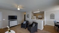 Located at 160 Peaceful Ln in Sanford, North Carolina, this single-floor residence offers a thoughtfully designed layout that maximizes comfort and functionality. The living area is carpeted and well-lit, featuring a ceiling fan with light fixture that enhances airflow and ambiance. The space accommodates furnishings comfortably and flows naturally into the kitchen area via an open pass-through layout, creating a connected and social atmosphere. The kitchen is defined by a raised breakfast bar-style counter that separates it from the living space while maintaining an open feel. Light wood cabinetry lines the kitchen walls, complemented by white appliances including a refrigerator, microwave, and electric range. Recessed and under-cabinet lighting add a warm, practical glow to the cooking area. The neutral color palette of whites and soft grays is carried throughout the space, contributing to a clean and inviting aesthetic. Transitions between carpet and hard flooring delineate the different functional areas. The overall design is practical and approachable, making this single-story Sanford home a well-organized and move-in ready residence suited for everyday living.