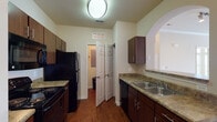 This single-floor residence is thoughtfully designed with a cohesive layout that balances function and comfort throughout. The galley-style kitchen is outfitted with dark espresso cabinetry, granite-look countertops, a double-basin sink, and black appliances, including a refrigerator, range, and dishwasher. Rich hardwood-style flooring runs through the kitchen and connects to adjacent areas, while a decorative arched pass-through opens the kitchen to the living space, enhancing the sense of openness and flow.

The living area is generously proportioned, featuring neutral carpet, crown molding, and a ceiling fan. An elegant arched opening frames the view into the kitchen, adding an architectural touch to the shared space.

The primary bedroom is well-sized, with soft carpet, a ceiling fan, and a bay-style window arrangement that fills the room with natural light and outdoor views. The primary bathroom offers dual sinks set into a long vanity with dark cabinetry, hardwood-style flooring, built-in open shelving, and direct access to a spacious walk-in closet equipped with wire shelving and hanging rods on multiple walls, providing substantial storage capacity throughout.