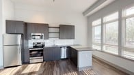 Located at 20 Water Grant Street in Yonkers, NY, this 2-bedroom, 2-bathroom residence offers a thoughtfully designed single-floor layout with modern finishes throughout. The open-concept kitchen is a standout feature, showcasing dark charcoal cabinetry, a white subway tile backsplash, stainless steel appliances including a range, microwave, dishwasher, and refrigerator, along with a peninsula that provides additional counter and prep space. Rich wood-tone flooring runs through the kitchen and living areas, complementing the contemporary aesthetic. The living area is bathed in natural light through a wide bank of windows and provides access to a private outdoor balcony via glass French doors. Both bedrooms feature plush carpeting and generous natural light; one includes a walk-in closet with built-in shelving. The two bathrooms are finished with clean, modern details — one includes a glass-enclosed walk-in shower with white subway tile and a dark-cabinetry vanity, while the second features a full tub-shower combination, a navy blue vanity with a white countertop, and wood-tone flooring. The neutral color palette and contemporary design create a cohesive, move-in-ready living environment.