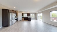 This single-floor unit showcases a thoughtfully designed open-concept layout that seamlessly connects the kitchen and living area. The kitchen is well-appointed with dark espresso cabinetry, light stone countertops, a herringbone tile backsplash, and a full suite of stainless steel appliances, including a refrigerator, range, over-the-range microwave, and dishwasher. A central island provides additional prep and storage space. Light-toned flooring extends throughout the main living area, complementing the neutral gray walls and textured ceiling. Recessed lighting ensures consistent illumination across the open space.

Large windows along the kitchen wall invite generous natural light, while a sliding glass door opens to a private balcony with outdoor views of surrounding greenery. The bedroom features plush carpeting and neutral walls, offering a calm and comfortable retreat. The bathroom is finished with dark vanity cabinetry, a white quartz countertop, a large mirror, and elegant marble-style tile flooring. A dedicated in-unit laundry area accommodates a full-size washer and dryer with overhead shelving for added convenience. Overall, the space presents a clean, modern aesthetic with practical, well-integrated features.