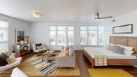 This single-floor unit is designed with an open-concept layout that seamlessly integrates the living, sleeping, and dining areas into one cohesive, light-filled space. A bank of large windows along one wall floods the main living area with abundant natural light and offers views of the surrounding neighborhood. Warm hardwood flooring runs throughout, complementing the clean white walls and providing a sense of continuity across the space. A ceiling fan and flush-mount lighting fixtures keep the area comfortable and well-lit.

The kitchen is thoughtfully designed with two-tone cabinetry — white upper cabinets paired with light wood-finish lower cabinets — set against a classic white subway tile backsplash. Dark granite countertops provide contrast, while stainless steel appliances, including a refrigerator, range, microwave, and dishwasher, complete the modern finish.

The entryway serves as a defined transition into the unit, featuring rich hardwood floors, recessed lighting, and ample wall space suited for art display.

The bathroom is clean and functional, featuring granite countertops, an undermount sink, a backlit mirror, and a full tub-shower combination with white tile surround and chrome fixtures.
