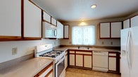 This single-floor, 2-bedroom, 2-bathroom home offers a practical and comfortable layout designed for everyday living. The kitchen is well-appointed with white cabinetry trimmed in warm wood accents, laminate countertops, and a full suite of white appliances including a gas range, over-the-range microwave, dishwasher, and a side-by-side refrigerator. Tile flooring and multiple windows with blinds keep the space bright and easy to maintain. A dedicated laundry room houses a full-size GE top-loading washer and dryer, complete with a window and wire shelving for additional storage. The living area features carpeted flooring and a set of sliding glass doors with vertical blinds, offering a direct view of lush outdoor greenery. Both bedrooms are carpeted and provide comfortable proportions; one includes a sliding-door closet with built-in wire shelving. The two bathrooms are cleanly finished — one features a soaking tub with tile surround and a single-sink vanity, while the second offers a walk-in shower with a glass door and a white vanity with updated fixtures. Throughout the home, neutral tones and consistent finishes create a cohesive, move-in-ready atmosphere.