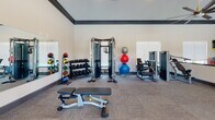 Located on Bridgewater Drive in Clarksville, Tennessee, this single-story community amenity center is designed to support both active lifestyles and family-friendly programming. The space is defined by consistent architectural details throughout, including bold dark crown molding that contrasts with light-toned walls, elevated ceilings, and neutral carpeted flooring that lends a clean, cohesive feel.

The fitness area is the centerpiece of the facility and is divided into two well-appointed zones. The cardio section is lined with multiple treadmills, stationary bikes, and a stair climber, accompanied by wall-mounted flat-screen TVs and windows that bring in natural light. Adjacent to this is a dedicated strength training area outfitted with a cable crossover machine, a full rack of dumbbells, medicine balls, stability balls, a weight bench, and additional resistance equipment — all framed by large mirrors that enhance the sense of space.

A separate children's activity area provides a welcoming environment for younger visitors. It features a charming rustic wooden Dutch-door gate, a miniature playhouse, and a mounted TV, creating a safe and engaging space for children. Fire safety equipment is visible throughout, reflecting attentiveness to building standards. Together, these spaces offer a well-rounded community resource suited for residents of all ages.