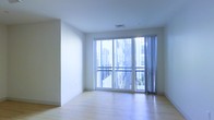 This contemporary single-floor space showcases a clean, minimalist design that emphasizes light and openness. The interior features smooth light hardwood flooring that runs throughout, complementing the crisp white walls and creating a bright, airy atmosphere. A ceiling-mounted HVAC vent reflects the modern infrastructure integrated seamlessly into the design.

The most striking architectural feature is the expansive floor-to-ceiling sliding glass door system, which floods the space with natural light and provides direct access to a private balcony. Sheer curtain panels frame the opening, offering a soft contrast to the clean architectural lines. The balcony is enclosed with a metal railing and offers views of the surrounding urban landscape, including neighboring buildings and a touch of greenery below.

The overall ambiance is calm and contemporary, with a neutral palette that provides a versatile canvas for a variety of uses. The open layout allows for flexible arrangement, while the abundance of natural light from the large glazed openings enhances the sense of spaciousness. This space is well-suited for those seeking a modern, light-filled environment in an urban setting.