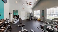 Located at 3900–3916 St Ives Rd in Myrtle Beach, South Carolina, this single-story fitness center is designed to provide a well-rounded workout environment. The space is defined by its vaulted ceilings, which lend an open, airy feel, and are complemented by recessed lighting and a ceiling fan that promote comfortable airflow during exercise sessions.

A standout design feature is the bold teal accent wall adorned with a lotus flower graphic and the word "BREATHE," creating a motivating and visually energetic atmosphere. Full-length mirrors along one wall visually expand the space and allow users to monitor their form during workouts. The dark rubber flooring throughout provides durability and safety underfoot.

The facility is equipped with a variety of cardio machines, including multiple treadmills and a stationary bicycle, as well as a multi-station cable weight machine, an adjustable workout bench, a dumbbell rack with a range of free weights, and a stability ball. A wall-mounted flat-screen television adds to the experience. Large windows along one wall allow natural light to fill the room and provide views of the surrounding greenery, further enhancing the inviting and functional atmosphere of this community fitness space.