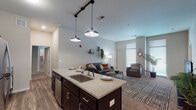 Located at 550 Pitt Greene Connector in Greenville, NC, this single-floor residential unit offers a thoughtfully designed open-concept layout that seamlessly connects the kitchen and living areas. The kitchen is a standout feature, showcasing dark espresso cabinetry, granite countertops, stainless steel appliances including a refrigerator, range, and built-in microwave, and a large central island with pendant lighting and bar seating — ideal for both meal prep and casual dining. Hardwood-style flooring anchors the kitchen and entry areas, transitioning to plush carpet in the living and bedroom spaces. The living room benefits from tall ceilings and large windows that invite abundant natural light, creating an open and airy atmosphere. Multiple bedrooms provide comfortable personal spaces, each carpeted and sized to accommodate a bed and study area. The bathrooms are finished consistently with dark vanity cabinetry, granite countertops, and wood-style flooring. A dedicated in-unit laundry room with full-size washer and dryer adds everyday convenience. The overall design reflects a modern aesthetic with neutral tones and quality finishes throughout, making it a well-appointed and functional living space.