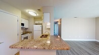 Located on Summerside Lane in Sarasota, Florida, this single-story unit offers a clean, functional layout with consistent finishes throughout. The living area is anchored by wood-style laminate flooring and a sliding glass door that opens to a private balcony with a railing, allowing natural light to fill the space and providing views of the surrounding landscape.

The kitchen is equipped with white cabinetry, a granite-topped peninsula with an undermount sink, a white refrigerator, electric range, and built-in microwave. The peninsula connects seamlessly to the living and dining areas, creating an open flow ideal for everyday use. A door from the kitchen provides additional access, likely leading to exterior or utility space.

A hallway connects the private areas of the unit, where wood-style flooring continues through the bedrooms. One bedroom features mirrored sliding closet doors and a sliding glass door with outdoor access. Another room offers a large window with vertical blinds, filling the space with natural light.

Two bathrooms share a cohesive design, each featuring granite countertops, white vanity cabinetry with brushed nickel hardware, and wood-look flooring. One bathroom includes a shower-tub combination with tile surround, while the other is configured as a half bath. Textured ceilings are present throughout the unit.