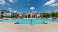 Located in Surf City, North Carolina, this pool house and amenity facility delivers a polished coastal retreat experience. The exterior centers around a expansive resort-style swimming pool with a spacious concrete surround, lounge chairs, and market umbrellas framed by palm trees beneath open Carolina skies. A charming hip-roof clubhouse structure anchors the pool area, featuring a covered porch with columns that seamlessly connects the indoor and outdoor spaces.

Inside, light-toned hardwood flooring and crisp white walls establish a clean, beach-inspired aesthetic throughout. The main gathering area is generously sized, featuring a fireplace as a central focal point, a wall-mounted flat-screen television, and a billiards table, making it ideal for socializing and recreation. Rattan lounge chairs with striped cushions add a casual coastal elegance, while framed artwork—including an oversized Scrabble board—gives the space a playful character.

A kitchenette area is outfitted with sage-green cabinetry, white quartz countertops, and stainless steel appliances, offering convenient poolside refreshments. Cozy nook seating areas are scattered throughout, including a quiet corner adorned with woven seahorse wall art and a round café table—perfect for casual conversation. Large windows and glass doors flood the interior with natural light and provide views of the lush surrounding greenery.