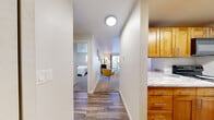 Park 212 is a thoughtfully laid-out one-bedroom, one-bathroom residence located in Edmonds, WA. The unit is organized on a single floor, offering a practical and comfortable flow throughout its spaces. A hardwood-style entry hallway connects the main areas, with the kitchen positioned conveniently to one side, featuring warm honey-toned cabinetry and marble-look countertops. The open living room is carpeted and well-lit, benefiting from a sliding glass door that brings in natural light and provides access to an outdoor area. The living space comfortably accommodates a seating area and media setup, with a ceiling fan adding to the room's functionality. The bedroom is a quiet, carpeted retreat with a bright window, offering a serene atmosphere. The full bathroom includes a tub-shower combination with clean, white surrounds and wood-style flooring. A dedicated laundry area houses a stacked GE washer and dryer unit, along with wire shelving for storage. An additional closet provides further organizational space. The overall palette throughout is neutral and bright, creating a clean and welcoming ambiance suited for everyday living.