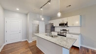 Located at 822 Williams Ave in Grandview Heights, Ohio, this well-appointed 2-bedroom, 1-bathroom residence offers a thoughtfully designed single-floor layout. The open-concept kitchen and living area forms the heart of the home, where rich hardwood-style flooring flows throughout. The kitchen is outfitted with stainless steel appliances, crisp white shaker cabinetry, granite-topped counters, and a central island with a built-in sink, accented by stylish pendant lighting on a track rail system. The spacious living room benefits from large windows that usher in generous natural light and views of the surrounding neighborhood. Both bedrooms feature soft carpeting and ample natural light, with the primary bedroom offering a walk-in closet equipped with wire shelving for organized storage. A second closet provides additional storage convenience. The full bathroom includes a glass-enclosed shower stall, wood-look flooring, and a white vanity with understated, clean finishes. Neutral wall tones and consistent trim work throughout the residence lend a cohesive, modern aesthetic, while a private exterior door off the living area provides added accessibility.