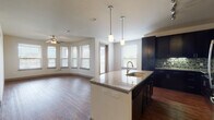 This single-floor residence showcases a thoughtfully designed open-concept layout that seamlessly connects the kitchen and living areas. The kitchen is a standout feature, offering rich dark cabinetry that extends to the ceiling, stainless steel appliances including a range, microwave, and refrigerator, and a striking mosaic tile backsplash. A generously sized curved island with granite countertops and an integrated sink serves as a natural centerpiece, complemented by stylish pendant lighting overhead. Warm hardwood flooring flows throughout the main living areas, while an abundance of windows dressed with blinds invites ample natural light and creates an open, airy atmosphere. Ceiling fans are present in the living and bedroom areas for added comfort. The bedrooms feature plush carpeting and good-sized windows with outdoor views, and closet space is well-considered. The primary bathroom is appointed with dual dark-cabinet vanities topped with granite, a separate walk-in shower, and large-format tile flooring. A secondary bathroom mirrors the refined aesthetic with a tub-shower combination and a granite-topped vanity. Throughout the space, neutral tones and consistent, high-quality finishes contribute to a cohesive and modern ambiance.