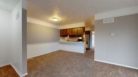 Located at 508–534 Long Blvd in Lansing, Michigan, this two-floor property offers a practical and functional layout across its main level and lower level. The main living area is open in concept, with neutral gray walls accented by white chair-rail molding and plush wall-to-wall carpeting that creates a warm, cohesive feel throughout. Large windows and a sliding glass door allow natural light to fill the space, contributing to an airy atmosphere.

The kitchen is positioned at the heart of the main floor and features rich, dark wood cabinetry, a white tile backsplash, and stainless steel appliances including a refrigerator and range. A peninsula counter connects the kitchen to the living area, offering a casual dining or workspace option. Hard wood-style flooring runs through the kitchen, providing a clean contrast to the carpeted surroundings.

The bathroom is well-appointed with a full tub and shower surround finished in white tile, a single vanity with dark wood cabinetry, and hardwood-style flooring. The lower level presents an unfinished basement with painted concrete floors, exposed joists, and in-unit laundry hookups, offering substantial additional storage or utility space.