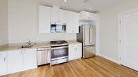 This single-floor unit offers a thoughtfully designed layout with a clean, contemporary aesthetic throughout. Warm-toned hardwood flooring flows seamlessly across all areas, providing a cohesive and inviting atmosphere.

The kitchen is a standout feature, outfitted with a full suite of stainless steel appliances including a gas range, dishwasher, built-in microwave, and a full-size refrigerator. Sleek white cabinetry extends to the ceiling, maximizing storage space, while a neutral-toned countertop with an integrated sink completes the functional workspace. Recessed lighting overhead keeps the area bright and practical.

The bathroom maintains the same modern sensibility, featuring light wood flooring, a white vanity with a marble-style countertop, a wall-mounted mirror, and clean white walls. A grab bar is mounted on the wall, adding an accessible touch to the design.

The hallway and adjoining areas are airy and open, benefiting from natural light streaming through a frosted floor-to-ceiling glass panel and a slatted window with blinds. Recessed ceiling lights and visible HVAC vents speak to the unit's functional infrastructure. The overall ambiance is bright, minimal, and move-in ready, with a neutral palette that provides a versatile backdrop for any interior style.