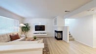 Located in Aliso Viejo, CA, this three-story home offers a thoughtfully designed layout spread across multiple levels. The entry level includes a private garage with an automatic opener, providing convenient direct access. The main living floor features an open-concept living, dining, and kitchen area anchored by light wood-style flooring and crisp white walls. The living room showcases a striking tiled corner fireplace and a sleek wall-mounted entertainment center, creating a warm yet modern focal point. The kitchen is equipped with white cabinetry, stainless steel appliances, a tile backsplash, and a granite-topped breakfast bar with seating — ideal for casual dining. Natural light flows freely throughout via multiple windows. The upper floor hosts two well-proportioned bedrooms, each featuring ceiling fans, light wood flooring, and ample natural light. The spacious primary bedroom includes a generous window bay and a dedicated closet. Five bathrooms serve the home, including clean, modern baths with frosted glass shower enclosures and white vanities. A patio extends the living space outdoors, while multiple staircases connect the floors efficiently. The home's cohesive light, airy aesthetic and multi-story design offer both comfort and functionality.
