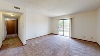 Located at 1000 S Basswood Cir in Bloomington, Indiana, this two-bedroom, one-bathroom unit offers a practical and well-organized single-floor layout. The kitchen is equipped with warm oak cabinetry, white appliances including a range, refrigerator, and built-in microwave, and features an extended white countertop peninsula that opens toward the living area — ideal for casual dining or additional workspace. The living room is generously sized with plush carpeting, a textured ceiling, and a sliding glass door that leads to a private balcony, filling the space with natural light and outdoor views. Both bedrooms are carpeted and well-proportioned, each featuring windows that bring in natural light. The primary bedroom is notably spacious and includes a large double-door closet and a ceiling fan with light fixture. The second bedroom offers a comfortable layout with its own window overlooking the surrounding greenery. Connecting these rooms are three hallways that provide a smooth flow throughout the unit. The bathroom includes an oak vanity with ample cabinet storage, a white countertop, a lighted mirror, and tile flooring. Neutral tones and consistent finishes throughout give this unit a cohesive and functional character.