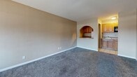 Located on Central Ave NE in Albuquerque, New Mexico, this single-floor, one-bedroom, one-bathroom unit offers a compact and functional layout across a single level. The living room is an open, carpeted space featuring neutral tan walls and a distinctive arched pass-through window that connects to the kitchen, adding a touch of architectural character. The kitchen itself includes wood-toned cabinetry and tile flooring, providing a warm contrast to the carpeted areas. The spacious primary bedroom is well-sized, featuring plush carpet, large windows with curtains that allow natural light and views of the surrounding landscape, and a wall-unit HVAC system. A built-in closet with a hanging rod offers practical storage directly off the bedroom, which also connects conveniently to the bathroom. The bathroom is finished with light tile flooring and tiled tub surround, complete with a shower-tub combo and chrome fixtures. Throughout the unit, textured walls and consistent neutral tones create a cohesive, understated aesthetic. The entry area transitions from tile to carpet, delineating spaces naturally. Windows throughout the unit bring in natural light and views of the New Mexico surroundings.