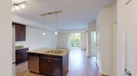 Located at 200 Hudson Court in Wheeling, Illinois, this one-bedroom unit offers a well-designed single-floor layout that maximizes functionality and comfort. The open-concept kitchen and living area serves as the heart of the home, featuring rich dark wood cabinetry, granite countertops, a large kitchen island with a double sink, stainless steel appliances, and stylish pendant lighting. Track lighting overhead adds a modern touch, while light hardwood-style flooring flows throughout the main living space, creating a warm and cohesive aesthetic. The living room is bright and airy, with sliding glass patio doors that invite natural light and provide views of the surrounding greenery, seamlessly connecting the interior to the outdoors. A dedicated entrance and hallway lead to the private bedroom, which is comfortably sized and finished with plush carpeting. The bedroom benefits from a large window that frames leafy outdoor views, contributing to a calm and restful atmosphere. A closet provides convenient storage. The unit's clean white walls and neutral palette create a versatile backdrop suitable for a variety of interior styles. With its thoughtful layout and quality finishes, this residence offers a practical and inviting living experience in Wheeling, IL.