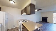 This single-floor unit offers a practical and functional layout designed for comfortable everyday living. The kitchen serves as a central feature, equipped with dark espresso-toned cabinetry, a peninsula counter with a light-toned laminate surface, a white electric coil range, dishwasher, and refrigerator. A ceiling fan with a light fixture overhead connects the kitchen to the open living area, which is finished with durable wood-look laminate flooring and a baseboard heating unit along the wall. The living space is bright and open, with clean white walls that enhance the sense of space.

A bedroom features carpeted flooring, a window with blinds that allows natural light, a baseboard heater, and a wall-mounted air conditioning unit for year-round climate control. A separate room with sliding glass doors and wood-look flooring offers additional versatile living space with access to the outdoors.

The bathroom includes a full tub and shower combination with tiled surround, a toilet, and a grab bar, finished in neutral tones. Throughout the unit, textured ceilings and neutral wall colors provide a clean, understated backdrop. The floor plan, as seen from the dollhouse view, presents a compact yet well-organized layout that efficiently utilizes the available space.