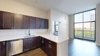 This 4-bedroom, 2-bathroom unit offers a thoughtfully designed single-floor layout that efficiently maximizes its footprint. The open-concept kitchen serves as a central hub, featuring rich dark-espresso cabinetry, white quartz countertops, a peninsula island, a stainless steel sink with a matte black faucet, a full suite of stainless steel appliances including a refrigerator, electric range, and microwave, and a classic subway tile backsplash. Dark hardwood-style flooring runs consistently throughout the living areas and bedrooms, providing a cohesive, modern aesthetic. The living area benefits from floor-to-ceiling windows and a sliding glass door that opens to a private balcony, flooding the space with natural light and offering open outdoor views. Each of the four bedrooms is well-proportioned, with large black-framed windows that continue the theme of natural light and exterior views. The two bathrooms are finished consistently, each offering dark vanity cabinetry, white quartz countertops, a single-sink vanity, a tub-shower combination with neutral tile surround, and light tile flooring. Two closets provide practical storage. The unit's neutral color palette of warm whites and soft grays creates a clean, modern ambiance throughout.