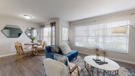 This single-floor residence offers a thoughtfully designed layout that balances comfort and functionality throughout. The open-concept living and dining area is anchored by large windows dressed with plantation shutters and curtain panels, flooding the space with abundant natural light and offering views of the surrounding greenery. Durable wood-look flooring runs through the main living areas, complementing the neutral gray wall tones and modern décor.

The kitchen is designed in a galley style, featuring white cabinetry with gold accent hardware, white countertops, a subway tile backsplash, a deep stainless steel sink with a matte black faucet, and stainless steel appliances including a refrigerator and electric range. Ample cabinet storage and a pantry closet enhance practicality.

The unit includes multiple bedrooms, each carpeted for warmth and comfort. The primary bedroom benefits from direct outdoor access through a sliding glass door, while additional bedrooms feature sliding closet doors and natural window light. Each bedroom offers generous closet space.

Two full bathrooms serve the unit, each outfitted with a shower-tub combination, white vanity cabinetry with gold hardware, and wood-look flooring. The clean, bright finishes throughout create a cohesive and inviting atmosphere across the entire residence.