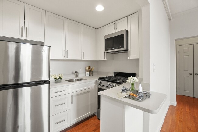 Modern kitchen with sleek stainless steel appliances, elegant white cabinetry, and warm hardwood floors, perfect for culinary enthusiasts. - Atrio Boston