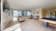 Located at 3450 Miller Dr in Chamblee, GA, this single-floor amenity space is thoughtfully designed to serve as a communal gathering and recreation area. The main living room is expansive and sun-drenched, featuring light hardwood-style flooring, crown molding, recessed lighting, and oversized black-framed windows that flood the interior with natural light and offer views of the surrounding community. Comfortable seating arrangements anchor the lounge area, complemented by a neutral, warm color palette throughout.

Adjacent to the lounge is a well-appointed game and entertainment zone, highlighted by a full-size shuffleboard table and a pool table, making it an ideal space for social gatherings. A built-in kitchenette with white cabinetry, a sink, microwave, and coffee station provides convenient refreshment access without a full kitchen footprint.

Large glass bi-fold or pivot doors open directly onto an outdoor terrace, seamlessly connecting the interior to an al fresco seating area with views of the pool and surrounding grounds. Two clean, modern restrooms with floating vanities, framed mirrors, and light wood-tone flooring complete the layout. A connecting hallway ties the spaces together efficiently, ensuring smooth circulation throughout this versatile and welcoming communal retreat.