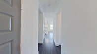 This well-appointed single-floor residence showcases a clean, modern aesthetic with a thoughtfully designed open-concept layout. Dark hardwood flooring flows seamlessly throughout the main living areas, creating a striking contrast against the bright white walls and trim.

The kitchen serves as the heart of the home, featuring white shaker-style cabinetry with matte black hardware, light granite countertops with subtle veining, and a classic subway tile backsplash. A peninsula with pendant lighting provides additional workspace and casual seating, while a large window above the sink fills the space with natural light. Stainless steel appliances, including a refrigerator with ice maker, range, and microwave, complete the kitchen.

The open living area is generously proportioned, with large windows and glass French doors leading to a private balcony, offering views of the surrounding neighborhood. A ceiling fan adds comfort to the space. A wide hallway connects the main living areas to the private rooms, which include carpeted bedrooms — one with its own balcony access. Two bathrooms serve the residence: a full bath with a tiled tub-shower combination and a double vanity, and a half bath featuring a single vanity with white cabinetry and matte black fixtures. The overall ambiance is bright, clean, and move-in ready.