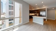 Located at 285 Molino Ave in Long Beach, California, this contemporary single-floor residence showcases a clean, modern design characterized by light wood-look flooring, soft neutral walls, and recessed lighting throughout. The open-concept living and kitchen area serves as the heart of the unit, where a large picture window floods the space with natural light and frames views of the surrounding urban streetscape, including a glimpse of palm trees that reflect the Southern California setting.

The kitchen is a standout feature, outfitted with rich dark wood cabinetry accented by brushed gold hardware, crisp white quartz countertops, a classic subway tile backsplash, and a full suite of stainless steel appliances. A generously sized kitchen island provides additional prep and seating space, seamlessly connecting the kitchen to the living area.

The hallway connects the main living spaces to the private areas of the unit, which include well-proportioned bedrooms, each benefiting from large windows that bring in abundant natural light. The bathrooms feature contemporary dark wood vanities with white countertops and gold-toned hardware accents. Closet space is notable, with walk-in and built-in storage options visible throughout. An in-unit laundry area with stacked units adds practical convenience to this polished, move-in-ready residence.