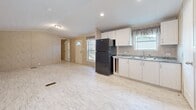 Located at 2214 E Fourth Ave in Hutchinson, Kansas, this single-floor, 3-bedroom, 2-bathroom home offers a practical and functional layout. The open kitchen serves as a central hub, featuring white cabinetry, a black refrigerator and range, a double sink with a granite-style countertop, and recessed lighting overhead. Light-toned vinyl flooring with a wood-like finish runs throughout the home, providing a cohesive and easy-to-maintain surface. The living area adjoins the kitchen in an open-concept fashion, with a front entry door flanked by windows that allow natural light to filter in. The bedrooms are finished with the same neutral, textured wall panels seen throughout the home, each offering closet space with wire shelving. The primary bedroom includes a window with a view of the outdoors, bringing in additional natural light. Both bathrooms are efficiently designed; one features a full tub-shower combo, a toilet, and a vanity with a granite-style countertop and mirror. The second bathroom offers a similarly appointed vanity. The home's consistent use of warm beige wall paneling and light flooring creates a neutral, cohesive interior palette throughout all rooms.