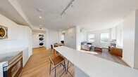 This well-appointed 3-bedroom, 2-bathroom unit in Calgary, AB offers a thoughtfully designed open-concept layout across a single floor. Light-toned hardwood flooring runs throughout, complementing the clean, white walls and recessed lighting that create a bright, contemporary atmosphere.

The combined kitchen, dining, and living area forms the heart of the unit. The galley-style kitchen is outfitted with stainless steel appliances, white flat-panel cabinetry, light quartz countertops, and a white subway tile backsplash. A breakfast bar provides additional seating and flows into the dining area. The living room benefits from large windows that invite generous natural light and offer open city views, with a wall-mounted mini-split air conditioning unit ensuring year-round comfort. A private balcony is accessible directly from the kitchen area.

The hallway, illuminated by recessed pot lights, connects the living spaces to the three bedrooms, each featuring hardwood floors, closets, and windows with city views. The two bathrooms are finished with white tile surrounds, soaker tub-shower combinations, and clean modern fixtures. A dedicated in-unit stacked washer and dryer adds everyday convenience, rounding out this functional and modern Calgary residence.