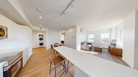 This well-appointed 3-bedroom, 2-bathroom unit in Calgary, AB offers a thoughtfully designed open-concept layout across a single floor. Light-toned hardwood flooring runs throughout, complementing the clean, white walls and recessed lighting that create a bright, contemporary atmosphere.

The combined kitchen, dining, and living area forms the heart of the unit. The galley-style kitchen is outfitted with stainless steel appliances, white flat-panel cabinetry, light quartz countertops, and a white subway tile backsplash. A breakfast bar provides additional seating and flows into the dining area. The living room benefits from large windows that invite generous natural light and offer open city views, with a wall-mounted mini-split air conditioning unit ensuring year-round comfort. A private balcony is accessible directly from the kitchen area.

The hallway, illuminated by recessed pot lights, connects the living spaces to the three bedrooms, each featuring hardwood floors, closets, and windows with city views. The two bathrooms are finished with white tile surrounds, soaker tub-shower combinations, and clean modern fixtures. A dedicated in-unit stacked washer and dryer adds everyday convenience, rounding out this functional and modern Calgary residence.