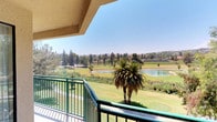 This single-floor space offers a seamless blend of comfort and scenic beauty, highlighted by a standout private balcony that serves as the crown jewel of the property. Framed by a textured stucco overhang and finished with green metal railings, the balcony opens up to a breathtaking panoramic view of a manicured golf course, complete with a tranquil pond, mature palm trees, and a dense tree line stretching across the background. Rolling hills in the distance complete the picturesque backdrop, all beneath an expansive, clear blue sky. The outdoor space is ideal for enjoying warm, sunny days in a peaceful natural setting. The lush greenery of the fairways creates a vibrant, resort-like atmosphere that permeates the entire space. Whether relaxing on the balcony or moving through the interior, residents benefit from the constant presence of this stunning landscape. The single-floor layout ensures easy accessibility and a cohesive living experience throughout. The combination of architectural detailing, natural light, and remarkable outdoor scenery makes this space a distinctive and inviting retreat with a strong connection to its surrounding environment.
