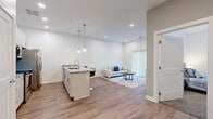 Located at 1866 E 93rd St in Cleveland, OH, this well-appointed one-bedroom, one-bathroom unit offers a thoughtfully designed open-concept layout with modern finishes throughout. Light-toned hardwood-style flooring flows seamlessly through the main living areas, creating a clean and cohesive aesthetic.

The kitchen is a standout feature, showcasing white cabinetry, granite countertops, stainless steel appliances including a French door refrigerator, electric range, and microwave, as well as a peninsula island with bar seating illuminated by sleek pendant lighting — ideal for casual dining or entertaining.

The kitchen opens directly into the living room, which benefits from natural light streaming through a large sliding glass door fitted with vertical blinds. The bedroom is carpeted for comfort, featuring windows with outdoor views and ample space for a full furnishing arrangement.

The bathroom maintains a clean, modern look with large-format tile flooring, a white vanity with storage drawers, a well-lit mirror, and a shower-tub combination. A dedicated in-unit laundry room with a stacked washer and dryer adds significant convenience. Recessed lighting and a neutral color palette of soft whites and warm grays tie the entire space together with a fresh, contemporary feel.