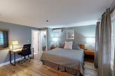 Located at 473 Main St in Barnstable, MA, this thoughtfully designed one-bedroom, one-bathroom space offers a comfortable and functional layout with a coastal aesthetic. The bedroom serves as the heart of the unit, featuring warm hardwood flooring, soft blue-gray walls, and a queen bed dressed in crisp, neutral bedding flanked by wooden nightstands with stylish table lamps. A wall-mounted split AC/heating unit ensures year-round climate comfort. Natural light filters in through windows dressed with layered curtains and blinds, providing a bright yet relaxed ambiance. A dedicated workspace with a desk and ergonomic chair adds practicality to the room. The bedroom also includes a walk-in closet with shelving and luggage storage. Along one wall, a media console houses a large flat-screen TV, mini-refrigerator, and microwave, complemented by a white barn-style cabinet offering additional storage and a coffee station. A framed mirror and decorative artwork complete the coastal-inspired décor. The private bathroom features classic white tile flooring with a red diamond accent pattern, a combined tub and shower, a single vanity, and a bright window that fills the space with natural light. This efficiently designed space offers a complete and comfortable retreat in the heart of Cape Cod.