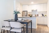 Located at 125 Canon Jackson Dr in Toronto's Mount Dennis neighbourhood, this thoughtfully designed one-bedroom, one-bathroom unit offers a clean, contemporary aesthetic throughout. The open-concept living and dining area is anchored by warm hardwood-style flooring and bathed in natural light from a glazed front entry door and adjacent windows, creating a bright and welcoming atmosphere. A compact dining area flows seamlessly into the living space, making efficient use of the layout.

The kitchen is a standout feature, showcasing floor-to-ceiling white cabinetry, a white subway tile backsplash, stainless steel appliances including a fridge and range, and a peninsula with a crisp quartz countertop that doubles as a breakfast bar. Recessed lighting overhead enhances the clean, modern finish.

The bedroom is a serene retreat with a tray ceiling detail, access to a private balcony through glass French doors, and in-unit stacked laundry conveniently tucked nearby. The bathroom features light tile flooring, a white vanity with integrated sink, and a large mirror that amplifies the sense of space. Throughout, the neutral white palette and natural wood tones create a cohesive, calming ambiance ideal for modern urban living.