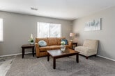 Located at 614 NE 38th St in Kansas City, Missouri, this single-floor residence offers a well-organized and functional layout across several distinct living spaces. The living room provides a welcoming atmosphere, featuring plush carpeting, neutral taupe walls, and a large window fitted with blinds that allows natural light to fill the space. The kitchen is efficiently designed with white cabinetry, laminate countertops, and white appliances including a refrigerator, range, and dishwasher. Stone-look tile flooring runs through the kitchen and connects to a dining area accommodating a bistro-style table and chairs. The primary bedroom is generously sized with soft carpeting, neutral walls, and a window providing natural light, offering ample room for a full bedroom suite. A second bedroom mirrors the understated design with carpet flooring, a window, and a built-in sliding closet for storage. The bathroom features tile flooring, a white vanity with under-cabinet storage, and a tub-shower combination. A security system panel is also present near the kitchen entry. Throughout, the residence maintains a cohesive, neutral color palette that creates a calm and practical living environment.