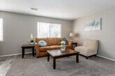 Located at 614 NE 38th St in Kansas City, Missouri, this single-floor residence offers a well-organized and functional layout across several distinct living spaces. The living room provides a welcoming atmosphere, featuring plush carpeting, neutral taupe walls, and a large window fitted with blinds that allows natural light to fill the space. The kitchen is efficiently designed with white cabinetry, laminate countertops, and white appliances including a refrigerator, range, and dishwasher. Stone-look tile flooring runs through the kitchen and connects to a dining area accommodating a bistro-style table and chairs. The primary bedroom is generously sized with soft carpeting, neutral walls, and a window providing natural light, offering ample room for a full bedroom suite. A second bedroom mirrors the understated design with carpet flooring, a window, and a built-in sliding closet for storage. The bathroom features tile flooring, a white vanity with under-cabinet storage, and a tub-shower combination. A security system panel is also present near the kitchen entry. Throughout, the residence maintains a cohesive, neutral color palette that creates a calm and practical living environment.