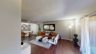 This single-floor residence offers a thoughtfully designed layout that balances comfort and style. The open-concept living area is a standout feature, showcasing rich hardwood flooring, a textured ceiling, and neutral-toned walls that create a warm, inviting atmosphere. The living room is anchored by a large framed wall mirror and accommodates generous seating, flowing seamlessly into a dedicated dining area with ceiling fan and ample natural light.

The galley-style kitchen is efficiently organized, featuring warm wood cabinetry, granite-style countertops, a double stainless steel sink, and white appliances including a refrigerator and range. A dedicated laundry area is conveniently accessible directly from the kitchen.

The primary bedroom offers a tranquil retreat with plush carpeting, natural light from large windows dressed with sheer curtains, and a tasteful accent wall. An additional bedroom provides a bright and playful space with dual windows, light carpeting, and a teal accent wall with built-in shelving.

The bathroom features a wood-framed vanity with granite-style countertop, a well-lit mirror, and hardwood flooring. The living space also includes a secondary seating area with sliding glass door access to the outdoors, offering a seamless indoor-outdoor connection. Throughout, the space maintains a cohesive, modern aesthetic with clean lines and contemporary furnishings.