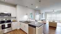 Located at 3600 Courtney Dr in Panama City, FL, this single-story residence offers a thoughtfully designed open-concept layout with clean, contemporary finishes throughout. Rich wood-look flooring flows through the main living areas, anchoring a bright and cohesive aesthetic defined by soft neutral tones and abundant natural light from multiple windows.

The kitchen serves as a functional centerpiece, outfitted with white shaker cabinetry, dark quartz countertops, a subway tile backsplash, and a full suite of stainless steel appliances including a refrigerator, range, microwave, and dishwasher. A large island with pendant lighting provides bar seating, seamlessly connecting the kitchen to the open living area. The living space is spacious and well-lit, with a ceiling fan and access to a private exterior door.

The bedrooms are generously sized with plush carpeting, ceiling fans, and wide windows dressed in blinds and curtains that offer natural light and privacy. The bathrooms are elegantly appointed with white cabinetry, dark quartz countertops, wood-look flooring, subway tile surrounds, and extended dual-vanity configurations. The primary bath leads to a walk-in closet, adding practical storage. Overall, the space presents a polished, modern living environment suited for comfortable everyday living.