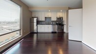 Located at 30 Front Street in downtown Hartford, Connecticut, this single-floor urban residence offers a sleek, modern aesthetic throughout. Rich, dark hardwood floors extend across the main living areas, reflecting natural light and lending warmth to the open layout. Large floor-to-ceiling windows frame sweeping views of the Hartford skyline, flooding the space with abundant natural light and creating a strong connection to the vibrant cityscape below.

The open-concept living area flows seamlessly into the kitchen, which is outfitted with white cabinetry, dark granite-style countertops, a striking mosaic tile backsplash, and a full suite of stainless steel appliances including a refrigerator, range, microwave, and dishwasher. Recessed lighting illuminates the kitchen workspace, complementing the sleek, contemporary design.

The bedroom area continues the hardwood flooring and offers generous proportions, with large windows providing additional city views and ample natural light. The bathroom is finished with large-format neutral tile flooring, a dark wood vanity with an integrated sink and mirror, and a tiled shower, offering a clean and functional space. Warm, neutral tones throughout create a cohesive and inviting ambiance suited to modern urban living.