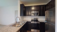 Located at 2581 Walcutt Rd in Hilliard, Ohio, this single-floor unit offers a well-designed layout with a cohesive modern aesthetic throughout. The kitchen is a standout feature, showcasing rich dark cabinetry that extends to the ceiling, granite countertops, a classic white subway tile backsplash, and a full suite of stainless steel appliances including a range, over-the-range microwave, and refrigerator. A double-basin stainless steel sink with a pull-down faucet completes the functional workspace. The kitchen opens to the main living area via a peninsula counter, creating an open and connected feel. The living space is bright and airy, with light-toned carpet, neutral white walls, and a sliding glass door fitted with vertical blinds that allows natural light to flow in. An adjacent room, accessible through an open doorway and accented by a chandelier, adds versatility to the layout. Bedrooms feature plush carpet flooring and large windows with blinds, allowing for ample natural light. The bathroom is clean and well-appointed, with dark wood-tone cabinetry, a white countertop vanity with a framed mirror, wood-look flooring, and a full soaking tub with a curved shower rod. The overall ambiance is fresh, modern, and move-in ready.
